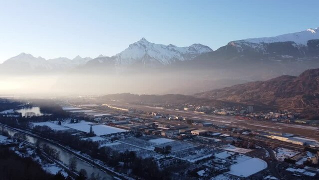 Drone flight against the light fog on the horizon over the town of Sion in the Swiss Valais in sunny weather and snow-capped mountains