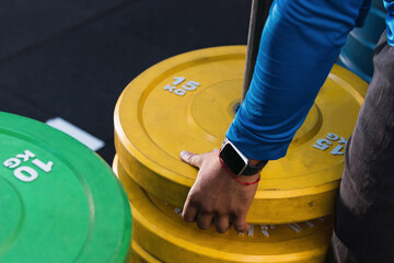 Hands of athlete removing weight plates in gym