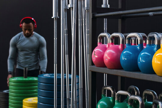 Colorful kettlebells and barbells stacked on rack with athlete in background in gym