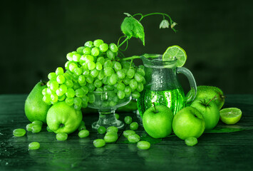 Beautiful still life with grapes, apples, pears and lemon. Lemonade in a transparent jug, green.