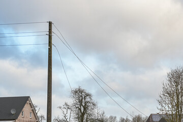 Concrete power pole with torn overhead transmission lines, storm damage in a rural village, cloudy...