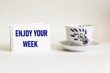 Notepad with words Enjoy the week on white background with vintage cup