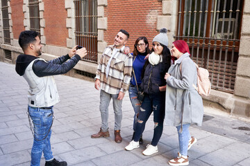 Obraz premium Latino man taking a picture with his smart phone of his group of friends on a city street. 