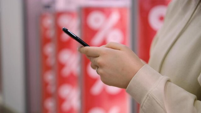 Flying the camera around. Red discounts. sale of goods.Girl holding her smartphone in her hands.pressing. Slow motion shot. A young girl with long nails stands in a shopping center near discount