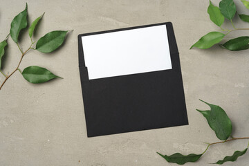 Paper envelope with white blank paper note and plant leaves on table