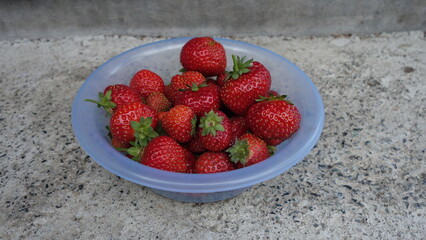 red strawberries in a plate on a gray background