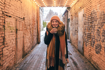 Naklejka premium Young woman in a hat, gloves, with a disposable cup of hot drink in winter.