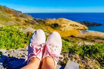 Fototapeta premium Female legs in sneakers against coast landscape, Spain.