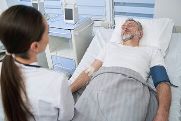 Calm patient undergoing intravenous therapy supervised by doctor