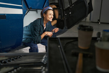 Caucasian woman mechanic in overall sitting on the jet airplane in hangar