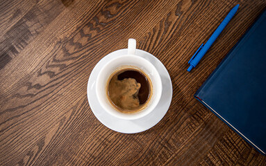 White cup of coffee on a saucer on a wooden table, top view.