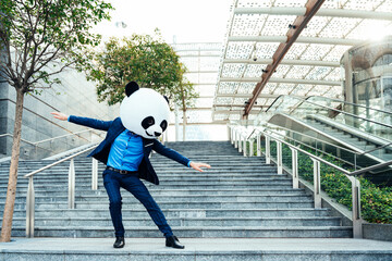 Storytelling image of a business man wearing a giant panda head. Funny cinematic concept about a crazy masked businessman traveling in the city center.