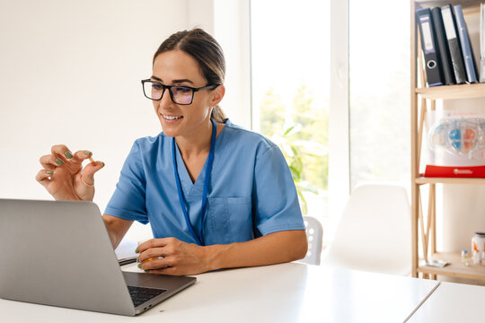 White woman doctor holding capsule while working with laptop