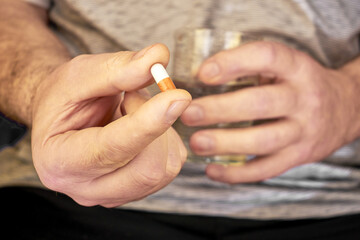 a man is holding a pill and a glass of water in his hands close-up