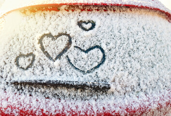 Four hearts (symbol of love) hand drawing on snow on the glass above windshield wiper of car....