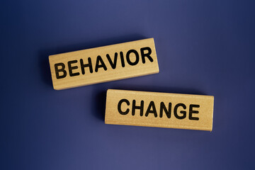 Wooden blocks form the words 'behavior change' on a dark blue background. Business concept