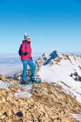 nice senior woman snowshoeing on the Nagelfluh mountain chain above a sea of fog over Bregenz Wald...