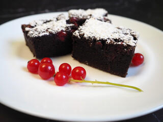 on a white plate on a black table are three pieces of gluten-free cakes with red currants, sprinkled with powdered sugar. gluten- and lactose-free cakes. homemade cakes with a diet