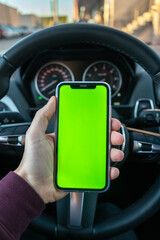 A vertical shot of a person inside his car looking at the mobile. Young man holding his mobile...