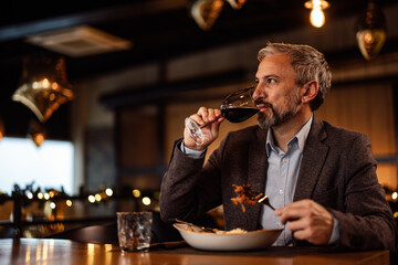 Concentrated caucasian adult sommelier, taste testing the wine, before taking a bite of food.