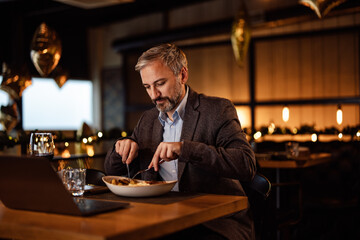 Concentrated adult man, making sure his food doesn't get cold while working on a laptop.