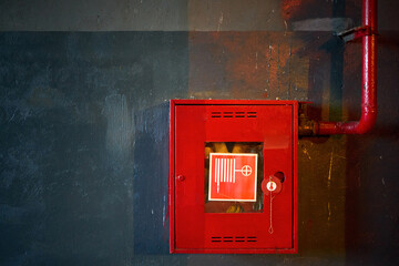 Fire hose in red box. Pipe roll for fire emergency in red metal cabinet on grey oil paint concrete wall with multicolor reflections as part of fire fighting system of industrial production plant.