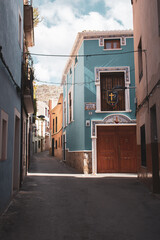 Fototapeta na wymiar Lonely street with colorful houses in the town of Villena, in the province of Alicante. Tight houses creating narrow and gloomy street. Street without people in the Valencian Community.