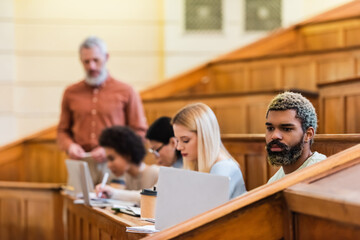 African american student using laptop near notebooks and coffee in university