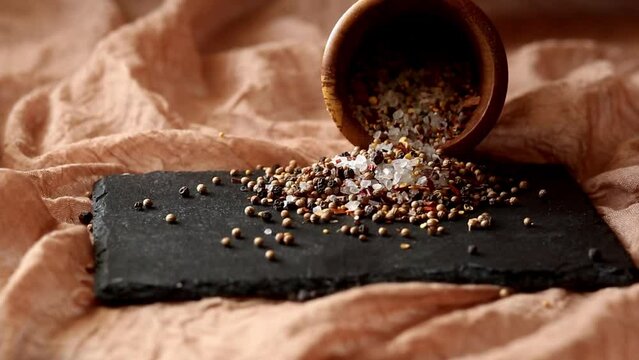 Seasoning - a mixture of pepper and coarse salt is poured from a mortar on a black board on a brown background. Adds flavor to food while cooking