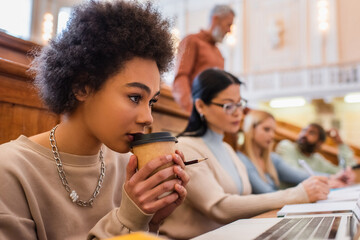 African american student holding coffee to go near laptop in university