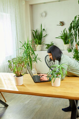 Woman florist with potted plant works on a laptop in flower plant shop