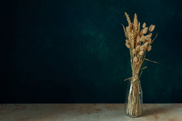 Bouquet of beautiful dried flowers in a glass vase on dark green blue background. Home decoration concept. Copyspace.