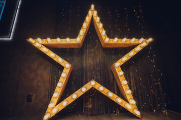 Photo of golden star with light bulbs on red velvet curtain on stage.