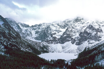 High winter mountains peak in Morskie Oko frozen lake in Poland with winter forest.