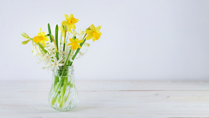 Yellow daffodils and white hyacinth flowers in crystal vase on wooden tabletop. Image with copy space