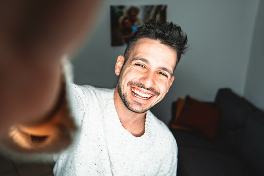 Young man taking selfie at home - Photo of handsome guy in living room enjoy weekend - Male dressed casual in video call laughing at camera	