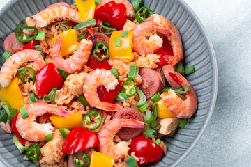 Jambalaya rice with chicken, shrimp, sausage and vegetables in plate on gray concrete table