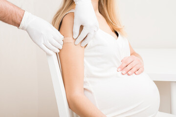Pregnant young woman visiting physician at office. Doctor hands in rubber protective gloves putting...