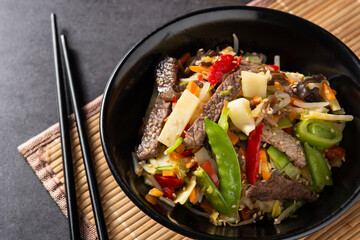 Beef, vegetables and sesame seeds in black bowl. Top view