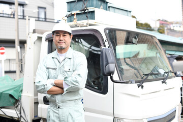トラックの前で腕組みをする作業服を着たミドル男性