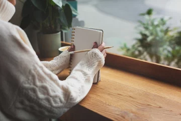 Unidentified woman is writing in the notepad in cafe. Working on bullet journal, diary, morning pages, plans and goals. Copy space for your text. © Yulia Lisitsa