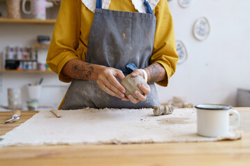 Female potter artist molding raw clay. Closeup of woman ceramist in dirty apron prepare for shaping pottery. Craftswoman hands work with earthenware. Art studio production and craftsmanship therapy