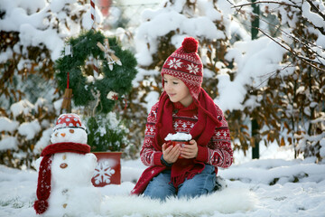 Sweet school child, boy, playing in garden with snow, making snowman, happy kid winter time