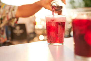 Cropped unrecognizable man serving fresh and cold red beverage on a sunny summer sunset