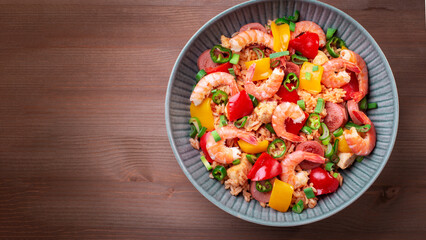 Jambalaya rice with chicken, shrimp, sausage and vegetables in plate on wooden table