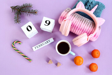 February 9 calendar: name of the month February in English, numbers 09, warm hat, headphones, a cup of coffee, sugar cubes, fruits and candies, pastel background, top view