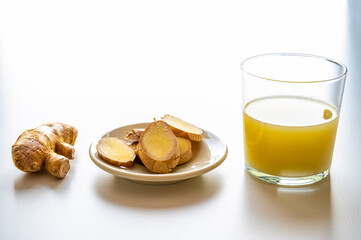 Ginger root, with pieces of ginger next to it and a glass of ginger juice. 