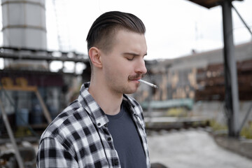 young handsome man with mustache in checkered black and white shirt smoking a cigarette outside....
