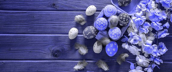 Painted Easter eggs with feathers and a branch of sakura on a Purple wooden background, border...