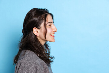 Fototapeta premium Profile view of cheerful young indian girl wearing gray pullover isolated on blue background. Concept of emotions, facial expression, youth, aspiration, sales
